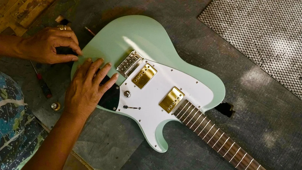mãos trabalhando na ponte de uma guitarra elétrica sobre a bancada, com os selins à mostra