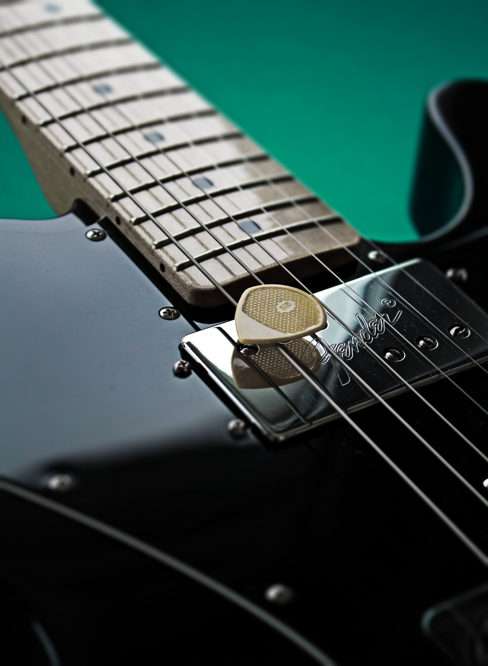 palheta apoiada nas cordas de uma guitarra elétrica, close no captador