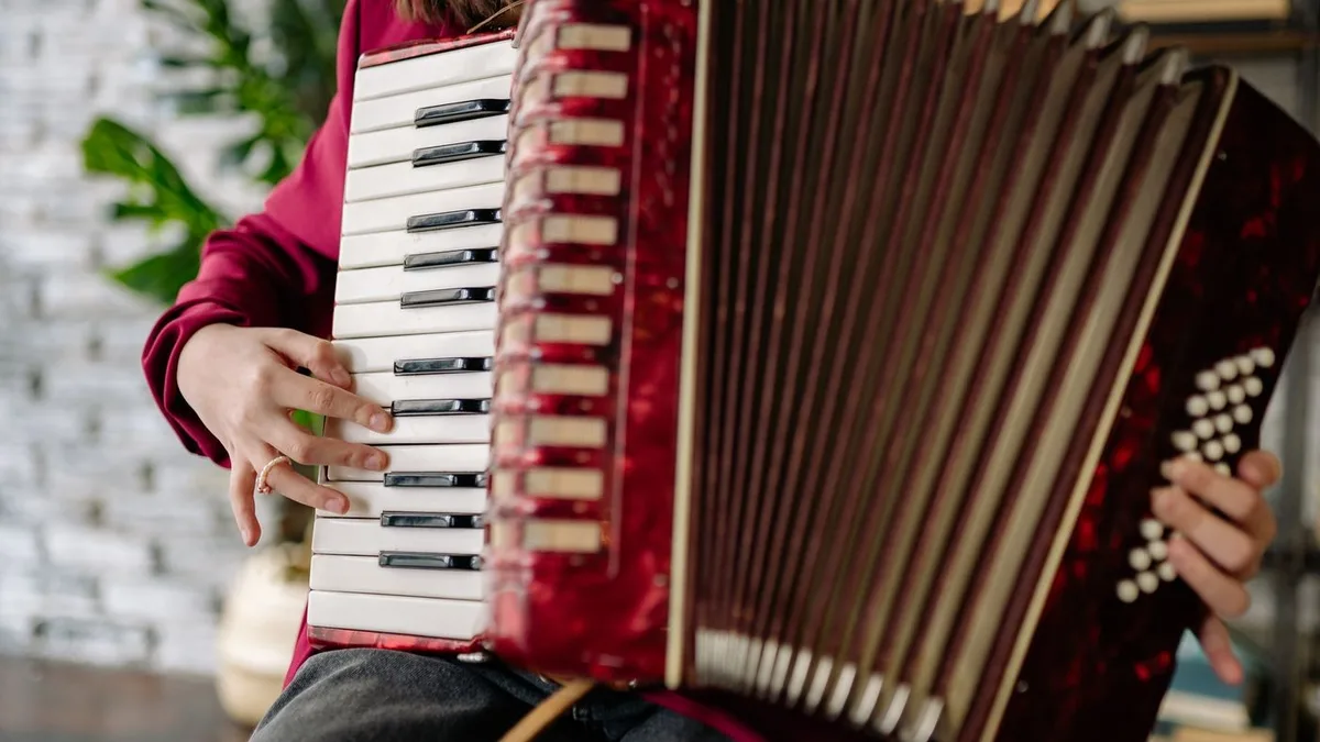 aluna de blusa vermelha tocando um acordeon de teclas com o fole aberto