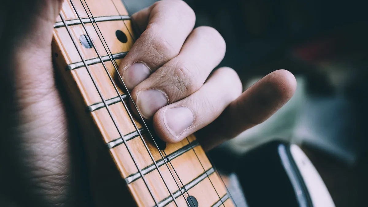 mão fazendo um acorde no braço de guitarra, com a escala em maple em primeiro plano