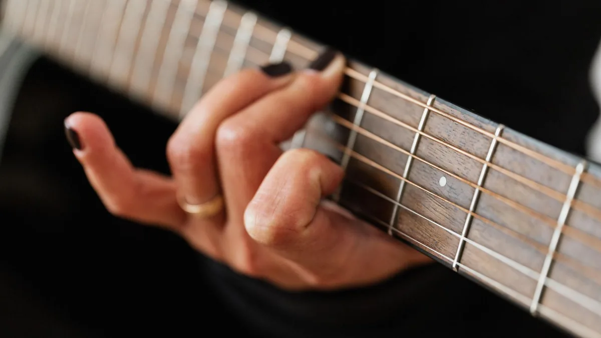 mão pressionando um acorde no braço da guitarra, com os dedos arqueados sobre as cordas