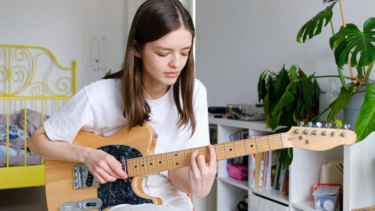 mulher tocando guitarra elétrica sentada em um quarto claro com plantas e estante