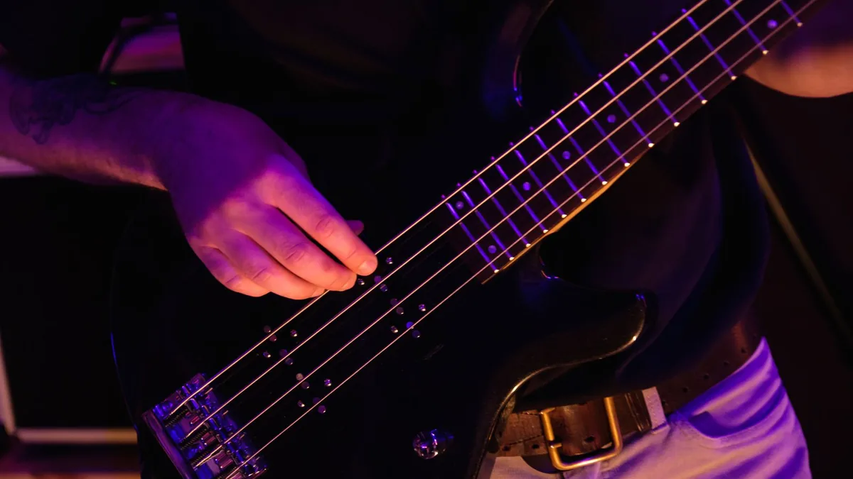 baixista tocando com os dedos um baixo preto de quatro cordas sob luz de palco