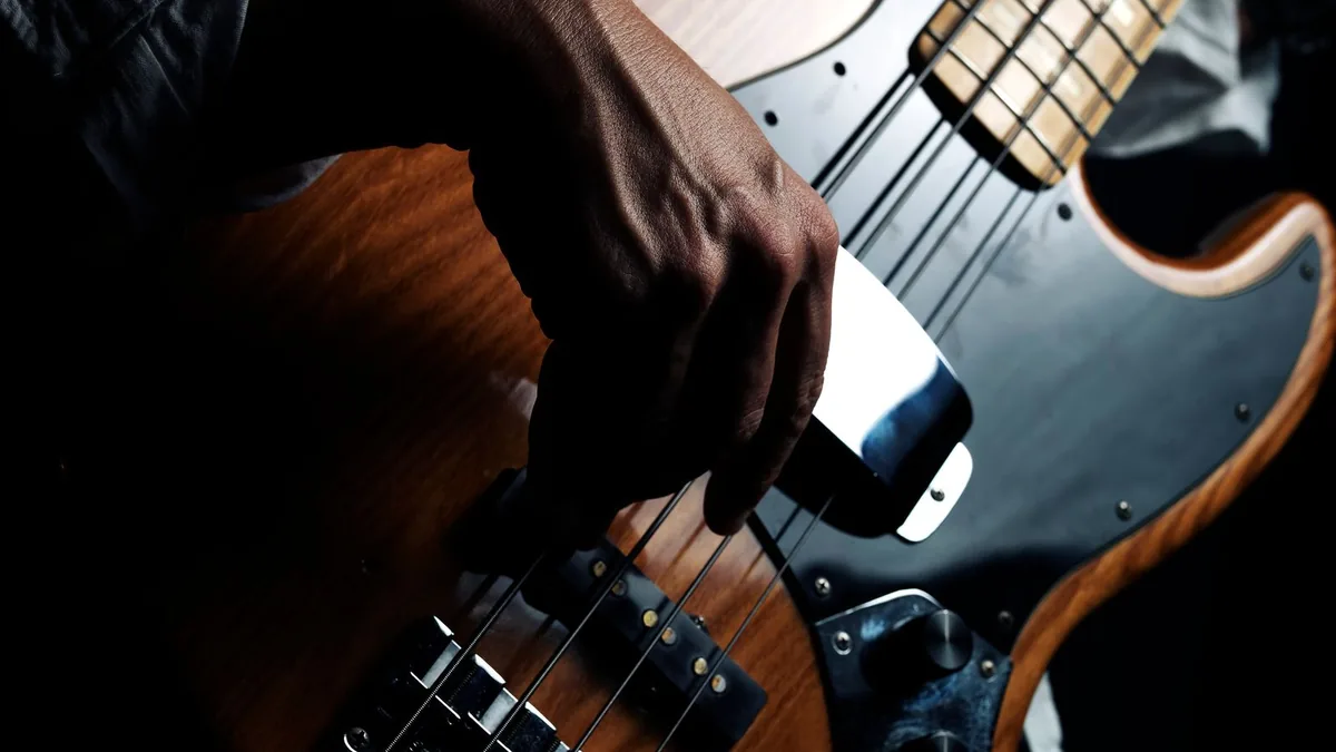 mão tocando de palheta um baixo de quatro cordas com corpo sunburst