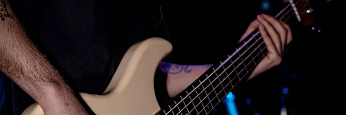 mão tocando o braço largo de um baixo de seis cordas em show