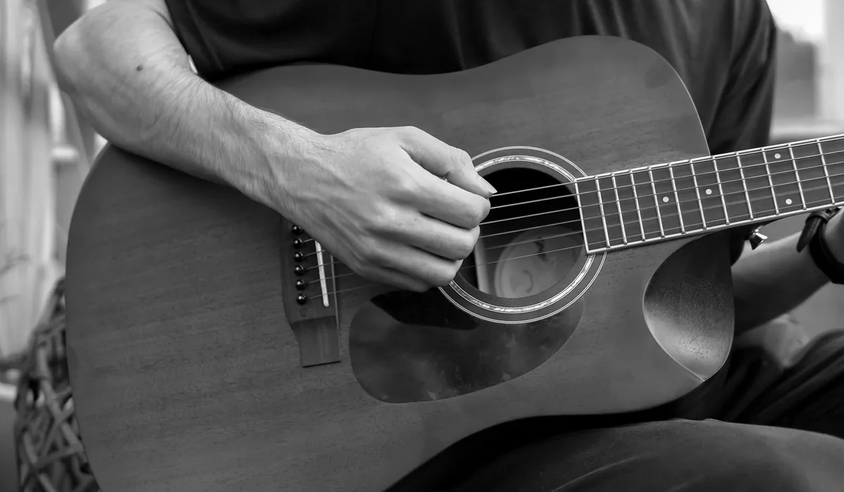 mão posicionando acorde no braço do violão durante estudo de harmonia
