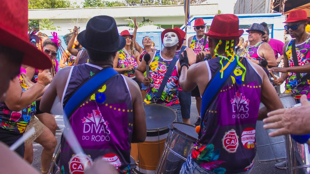bloco de rua com músicos de costas tocando tambores e instrumentos de percussão em um desfile colorido