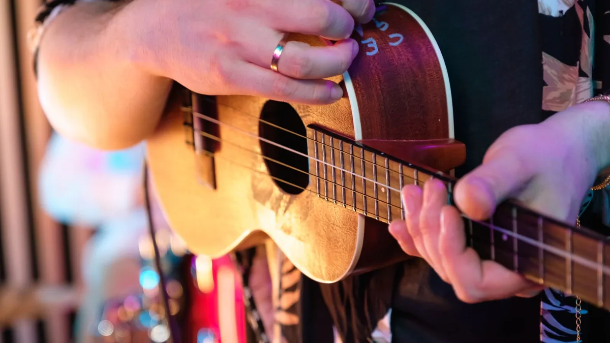 mãos de uma pessoa tocando um instrumento de cordas pequeno em um ambiente iluminado