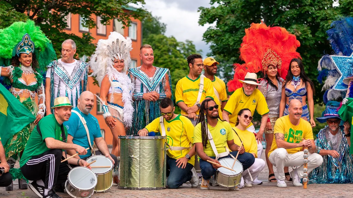 grupo de músicos de samba com camisas amarelas e verdes tocando tambores e surdos em uma praça