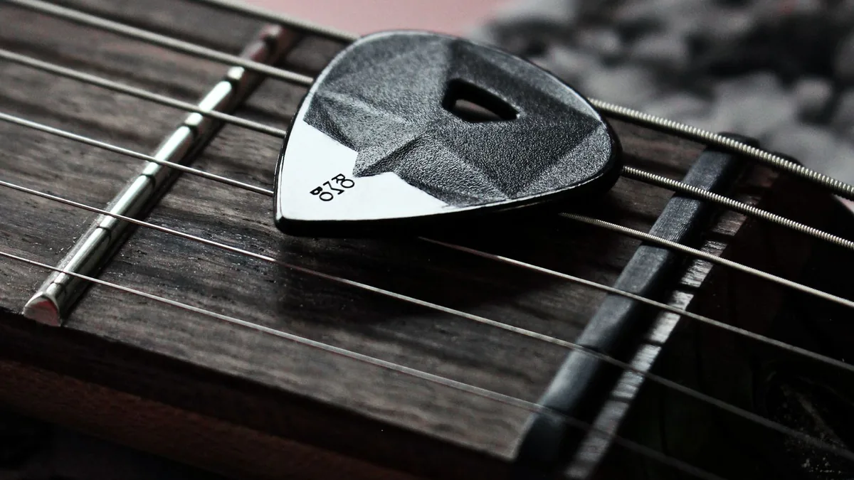 palheta apoiada sobre cordas de guitarra já sem brilho, na escala escura
