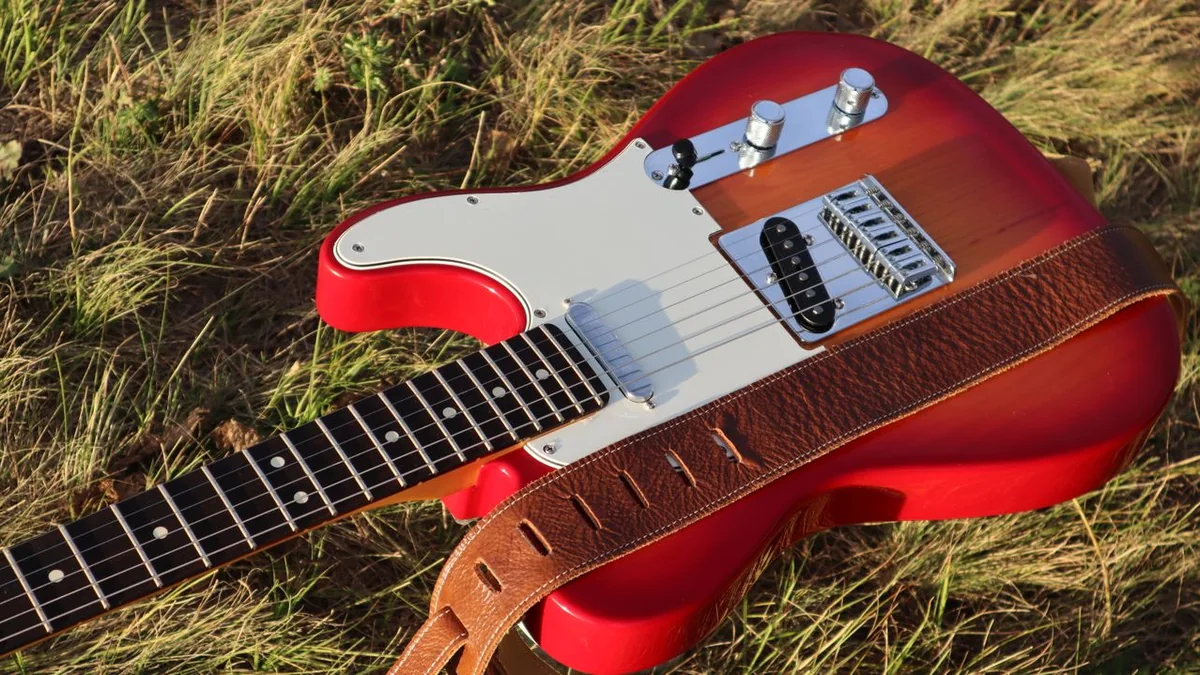 guitarra Telecaster vermelha deitada na grama com uma correia de couro marrom ao lado do corpo