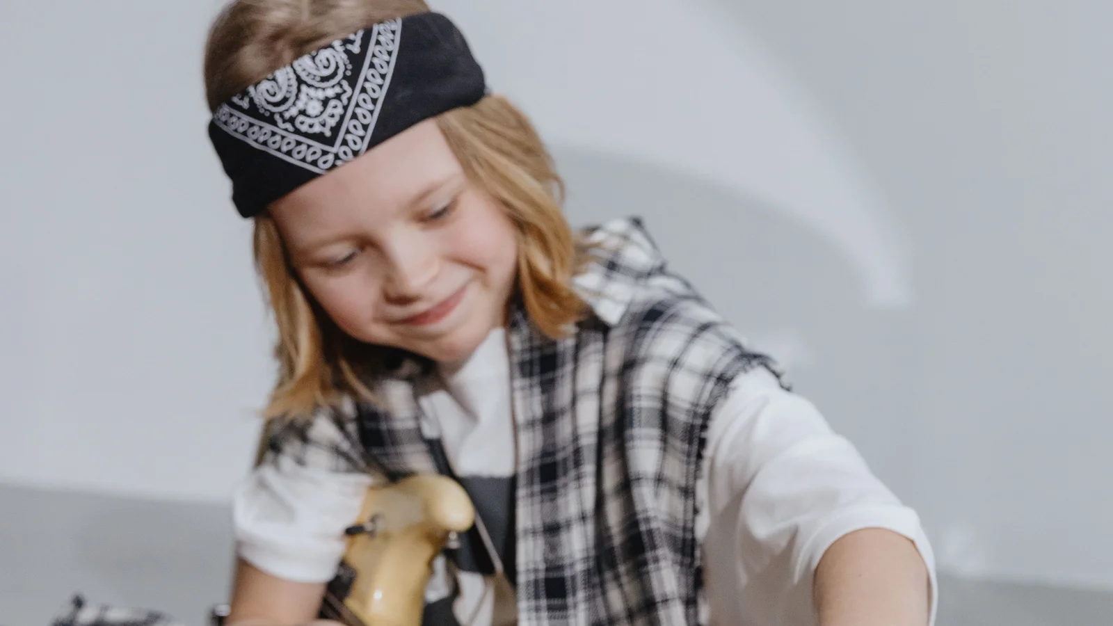 criança sentada ajustando as tarraxas de uma guitarra elétrica tamanho reduzido