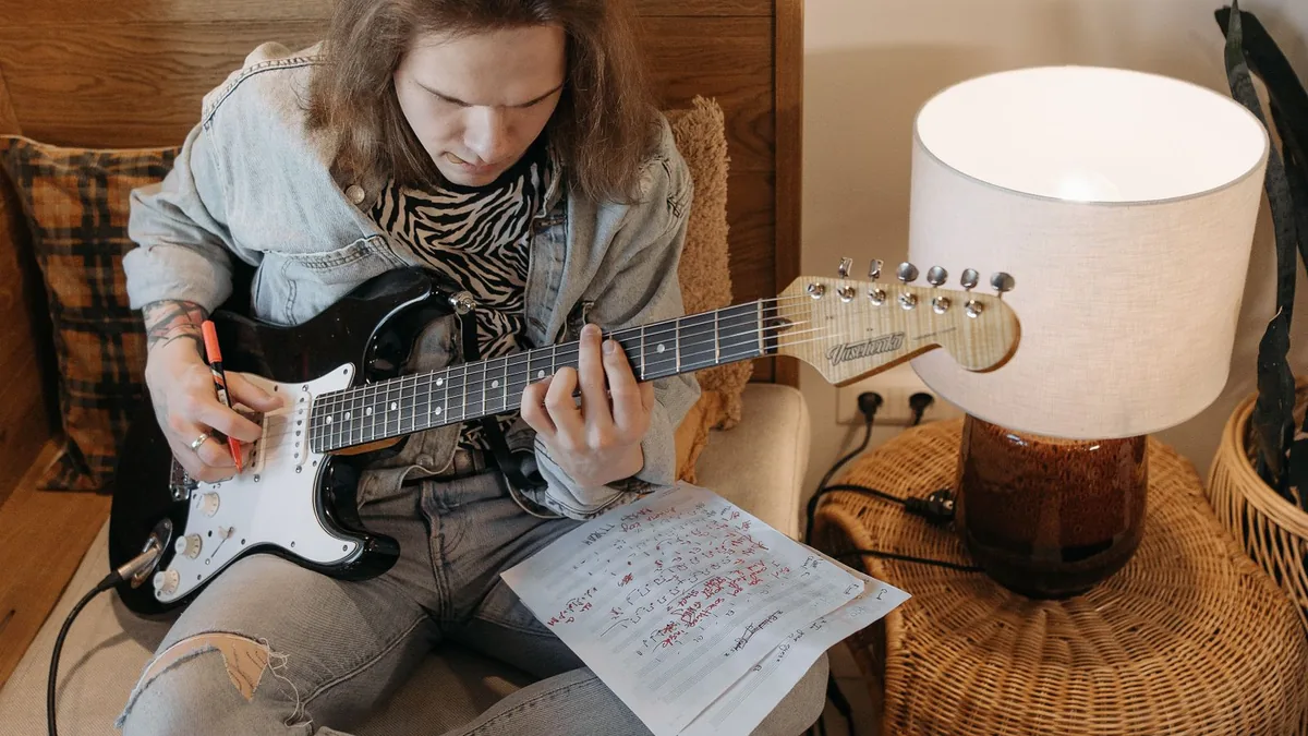 guitarrista com caneta na mão estudando a guitarra ao lado de anotações escritas