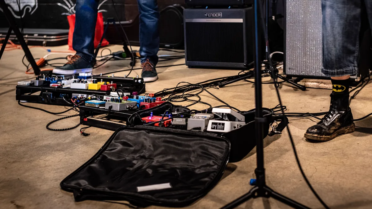 pedalboard sobre o palco com cabos de áudio e de energia passando entre os pedais