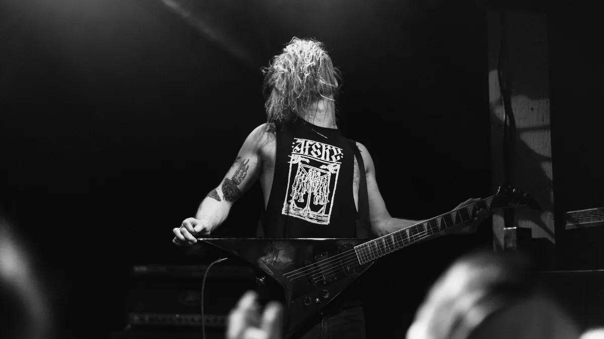 guitarrista de costas tocando em palco escuro, em foto preto e branco