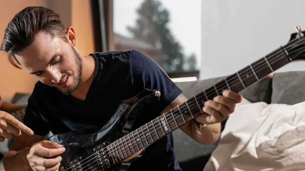 guitarrista sorrindo com as mãos no braço de uma guitarra elétrica, estudando