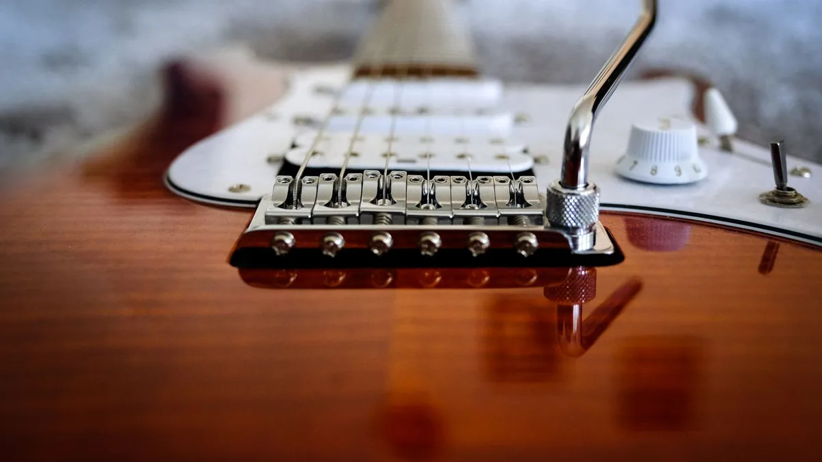 close da ponte com alavanca de trêmulo e pickguard branco de uma guitarra Stratocaster sunburst