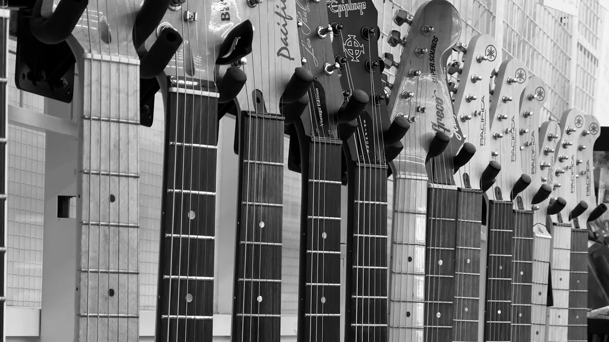 fileira de braços de guitarras elétricas penduradas em uma parede de loja, em preto e branco