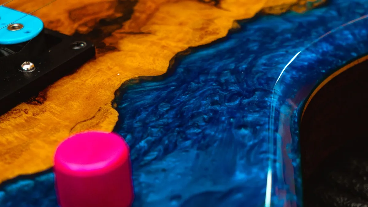 detalhe de corpo de guitarra com resina azul, madeira marrom e botões de volume rosa choque