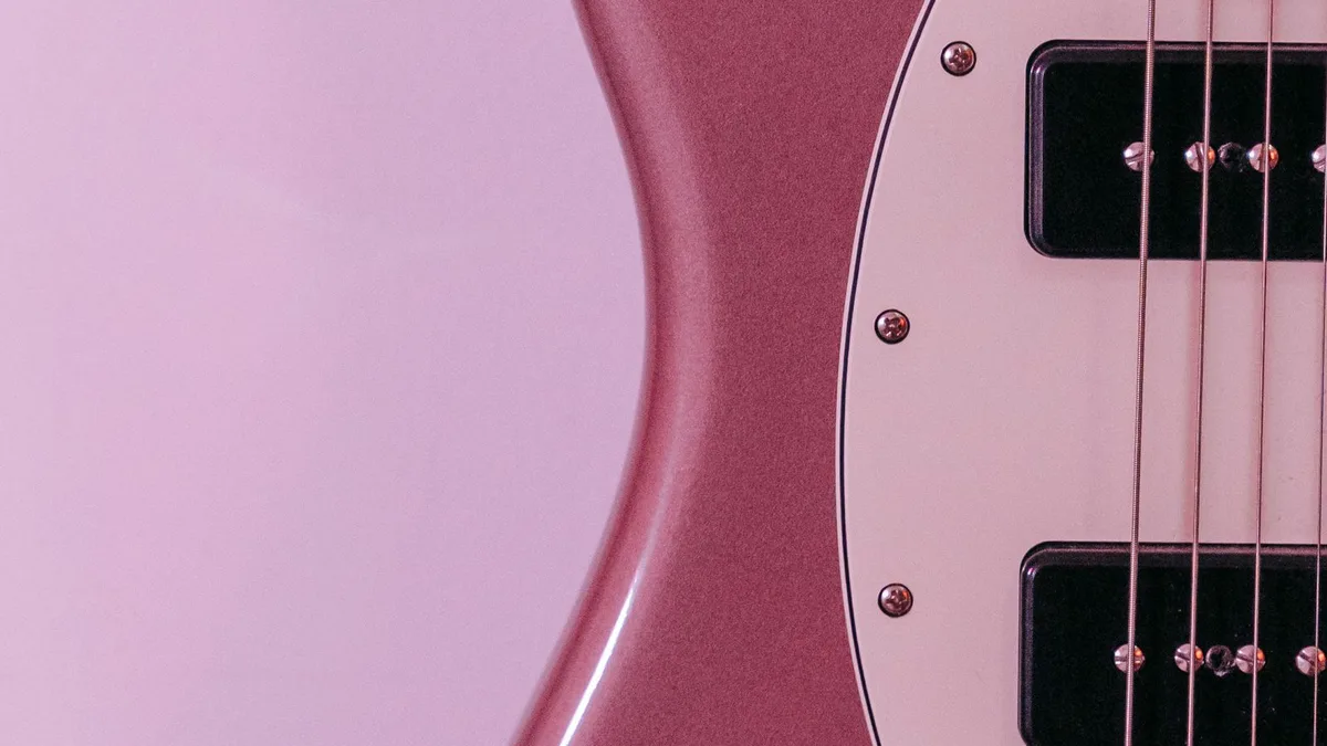 detalhe do corpo de uma guitarra rosa metálico com escudo branco, captadores pretos e cordas