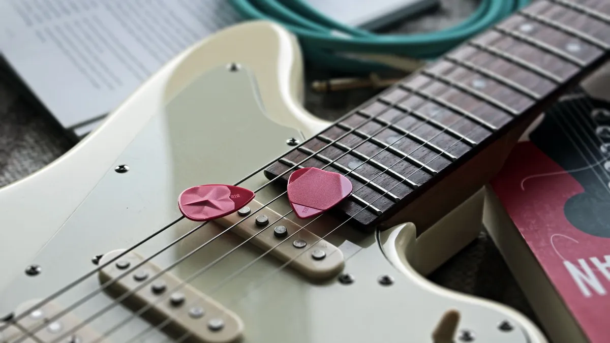 braço de guitarra branca com palhetas rosas sobre as cordas e cabo verde ao lado