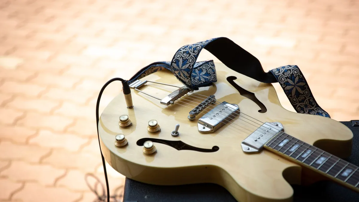 guitarra semi-acústica amarela com correia apoiada sobre um amplificador ao ar livre