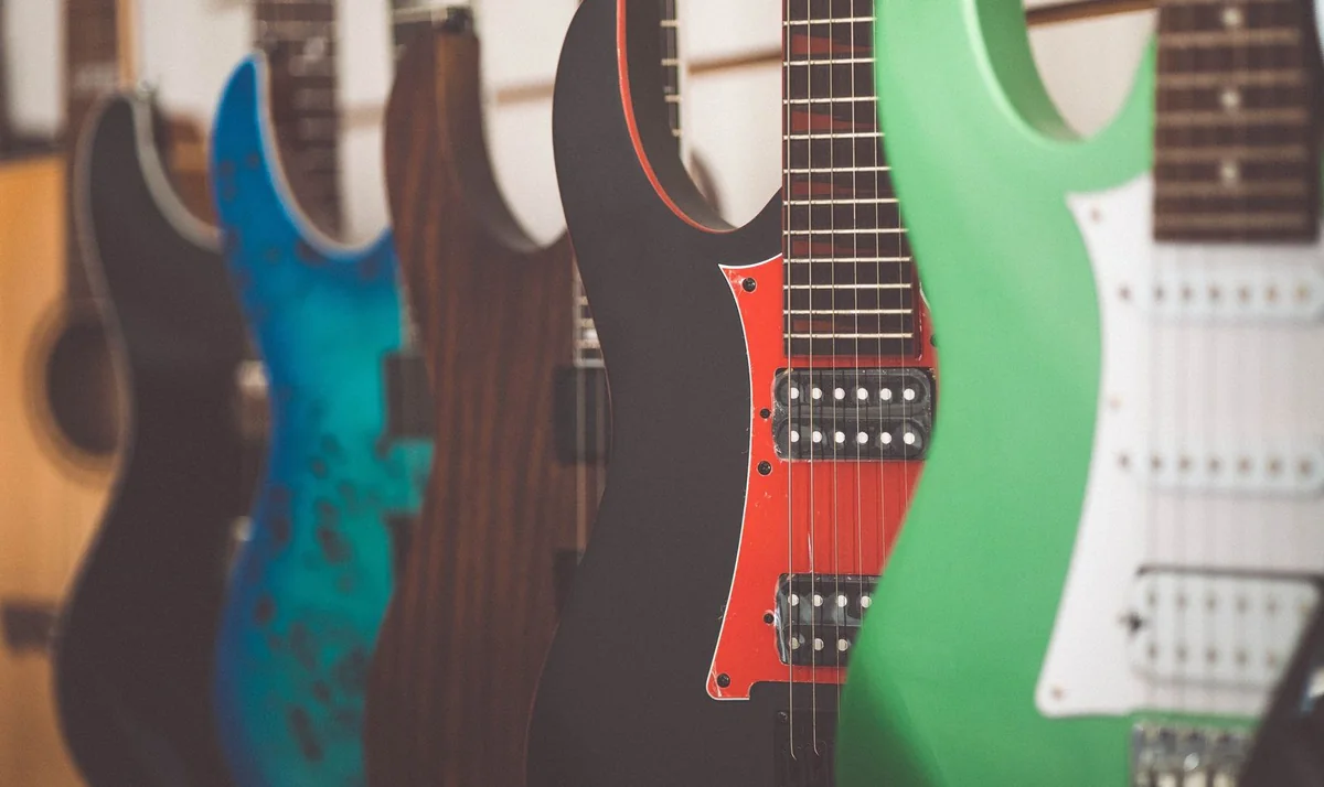 fileira de guitarras elétricas de cores diferentes, enfileiradas na parede de uma loja