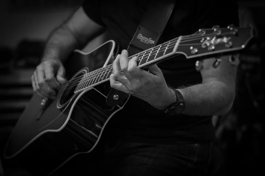 mãos posicionadas no braço de uma guitarra, close em preto e branco