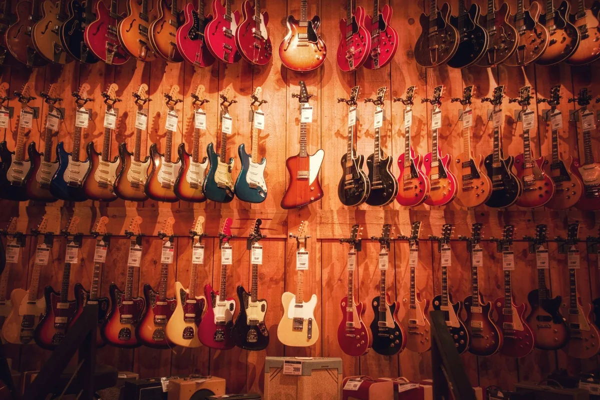 parede de loja de música com dezenas de guitarras penduradas e etiquetas de preço