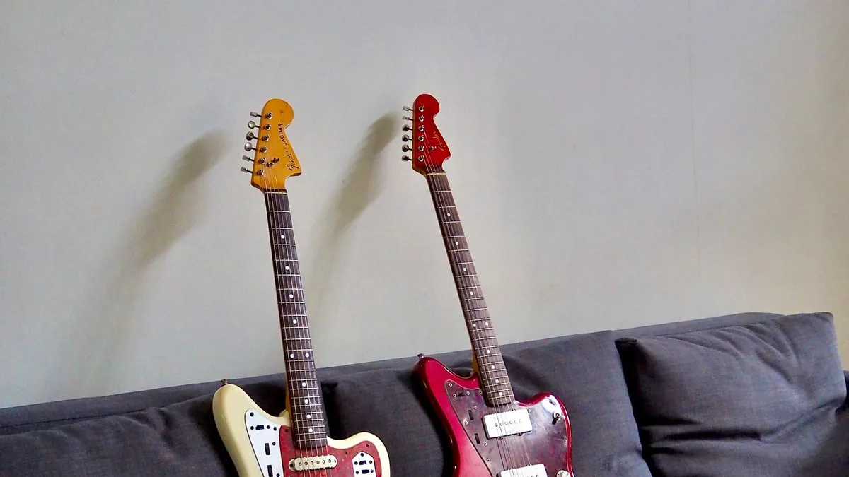 cabeças de uma Jaguar e de uma Jazzmaster encostadas na parede, com tarraxas e logotipo da Fender
