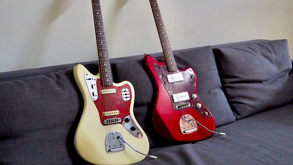 uma Jaguar creme e uma Jazzmaster vermelha apoiadas lado a lado em um sofá cinza