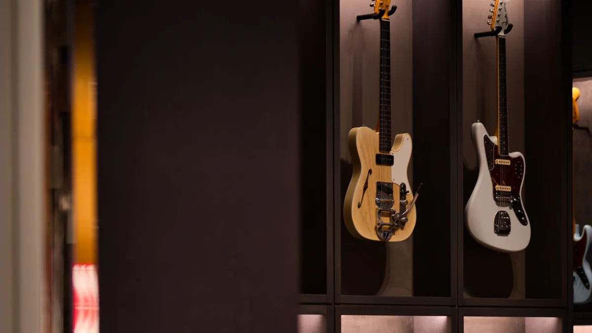 vitrine escura de loja com várias guitarras Fender penduradas, entre elas uma Jaguar branca e uma Telecaster