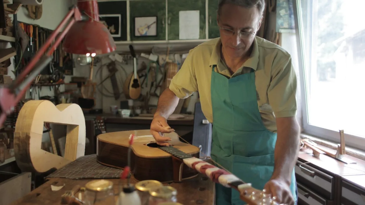 luthier trabalhando em um instrumento sobre a bancada, com ferramentas na parede da oficina