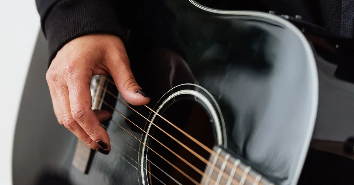 mão dedilhando violão de aço preto de perto