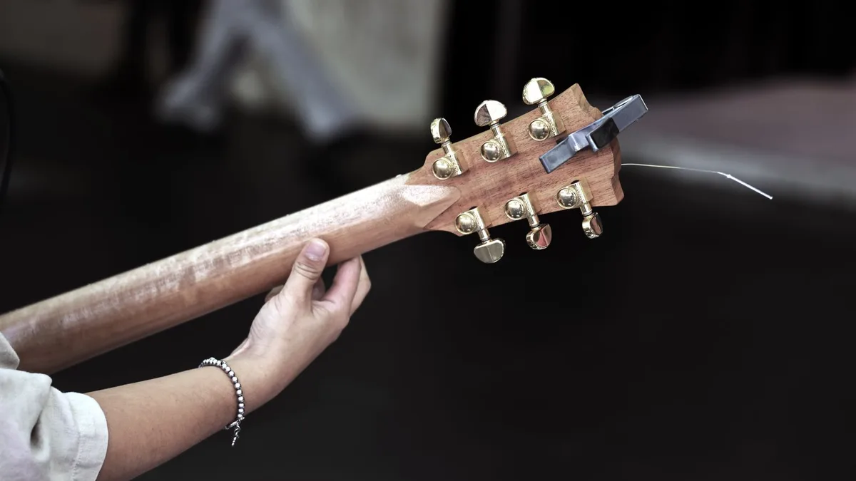 mãos girando a tarraxa de um violão para afinar uma corda