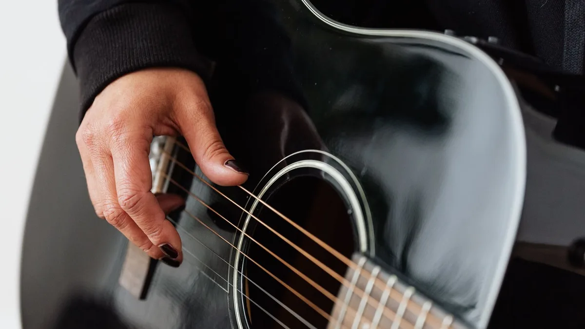 mão direita batendo as cordas de um violão preto