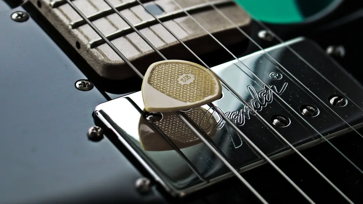 palheta bege apoiada sobre o captador de uma guitarra preta, com as cordas por cima
