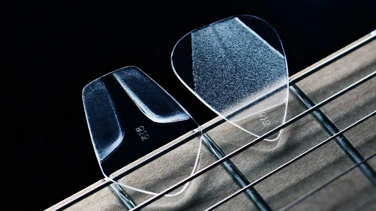 duas palhetas transparentes apoiadas sobre as cordas e a escala de uma guitarra