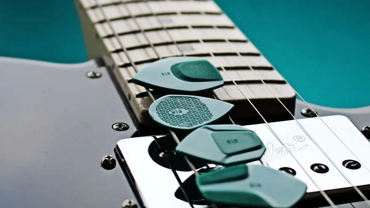 quatro palhetas verdes de formatos diferentes empilhadas sobre o captador de uma guitarra preta