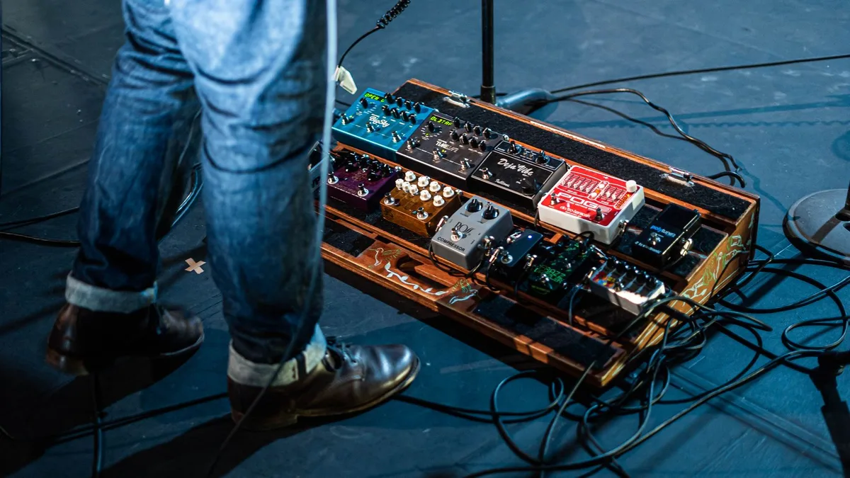 pedalboard iluminada em um palco, com os pés de um guitarrista ao lado de vários pedais