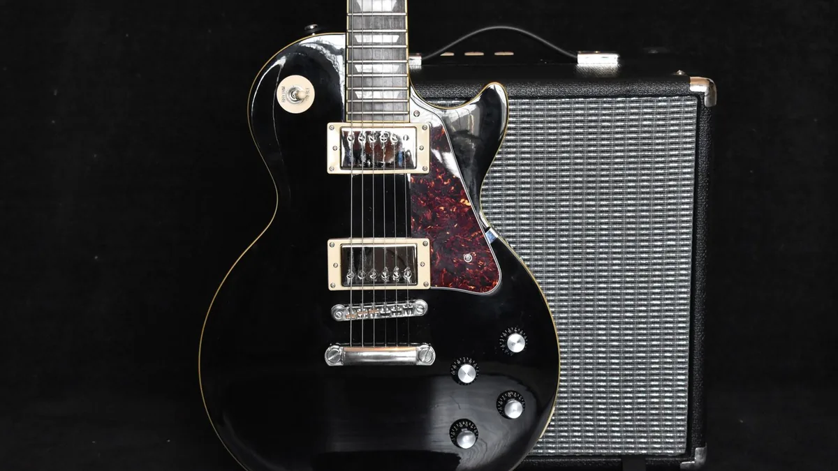 guitarra elétrica preta tipo Les Paul encostada em um amplificador pequeno sobre fundo escuro