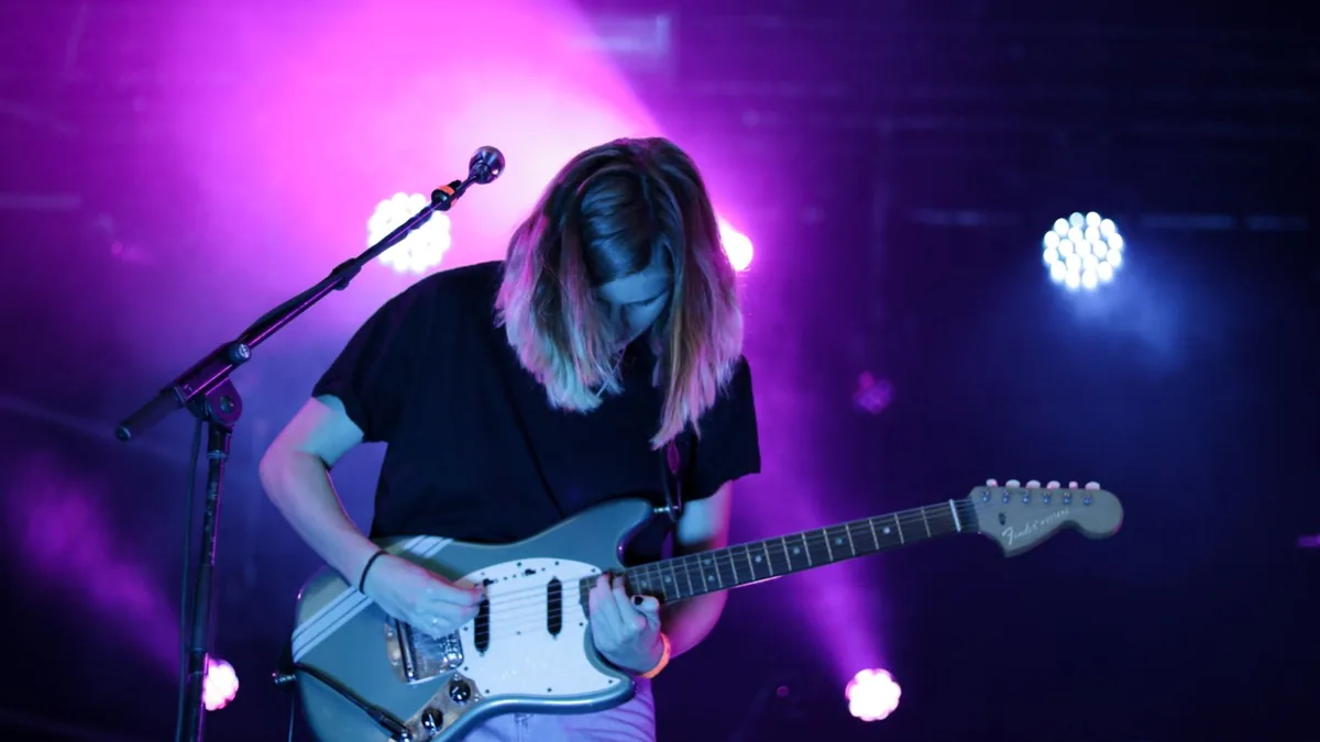 guitarrista tocando em um palco com luz roxa e guitarra azul clara