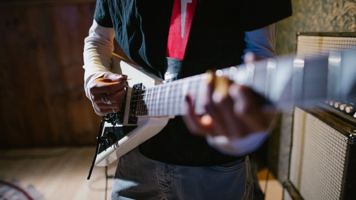 guitarrista segurando um power chord no braço de uma guitarra branca com amplificador ao fundo
