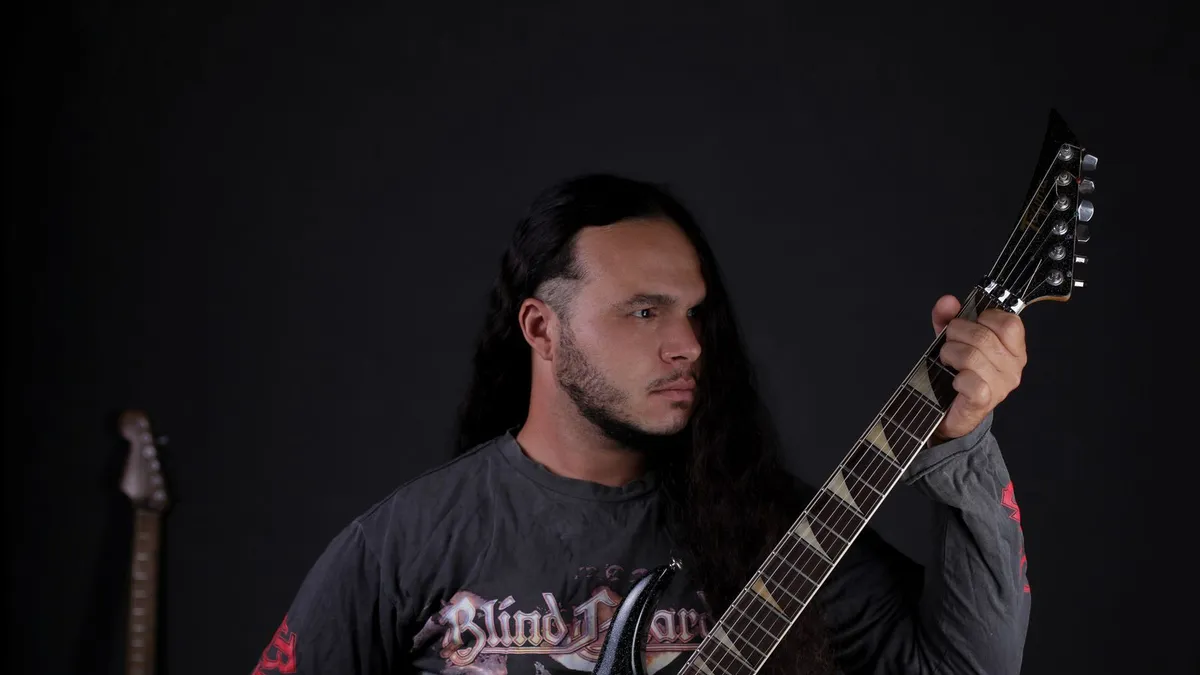 guitarrista de cabelo comprido segurando uma guitarra elétrica de braço longo em um fundo escuro