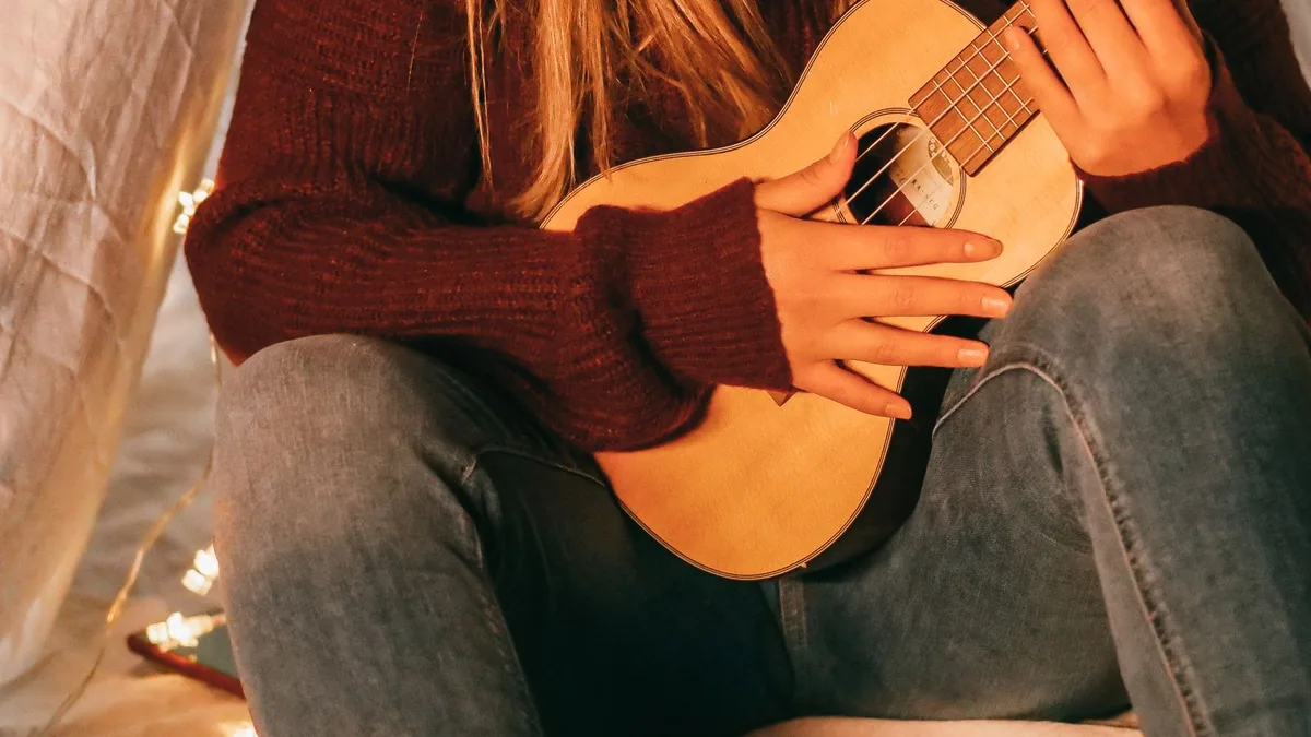 mulher sentada tocando um ukulele de madeira com o instrumento apoiado no colo