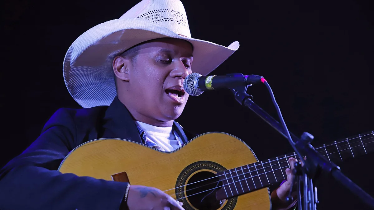 violeiro de chapéu cantando ao microfone enquanto toca uma viola caipira de corpo amarelo