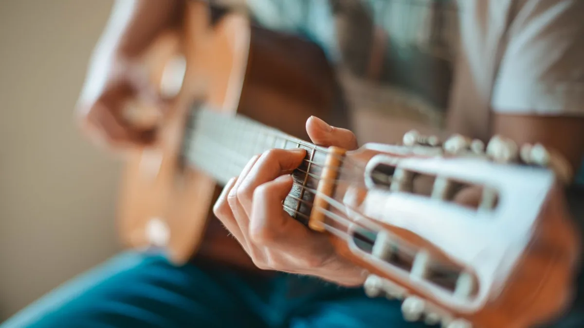 mão pressionando as cordas de um violão de nylon, com foco na cabeça fendida e nas tarraxas