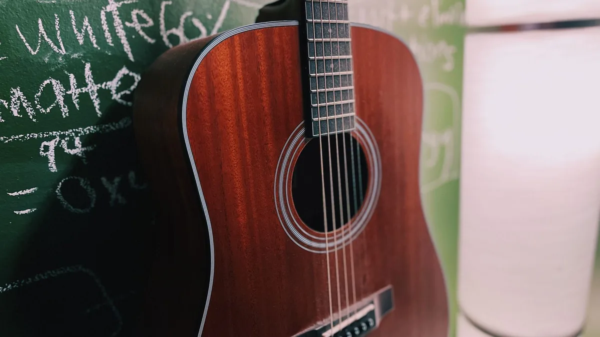 violão dreadnought de mogno avermelhado apoiado em uma parede de lousa verde