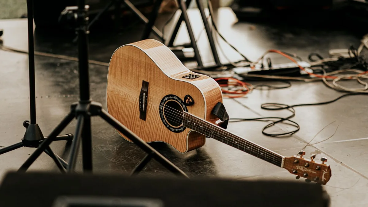 violão eletroacústico de cutaway deitado no chão de um palco entre cabos e pedestais