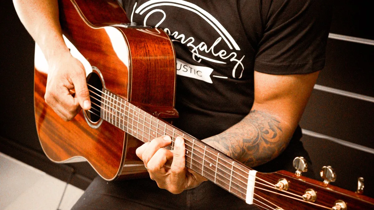 violonista de camiseta preta fazendo um acorde no braço de um violão folk de mogno